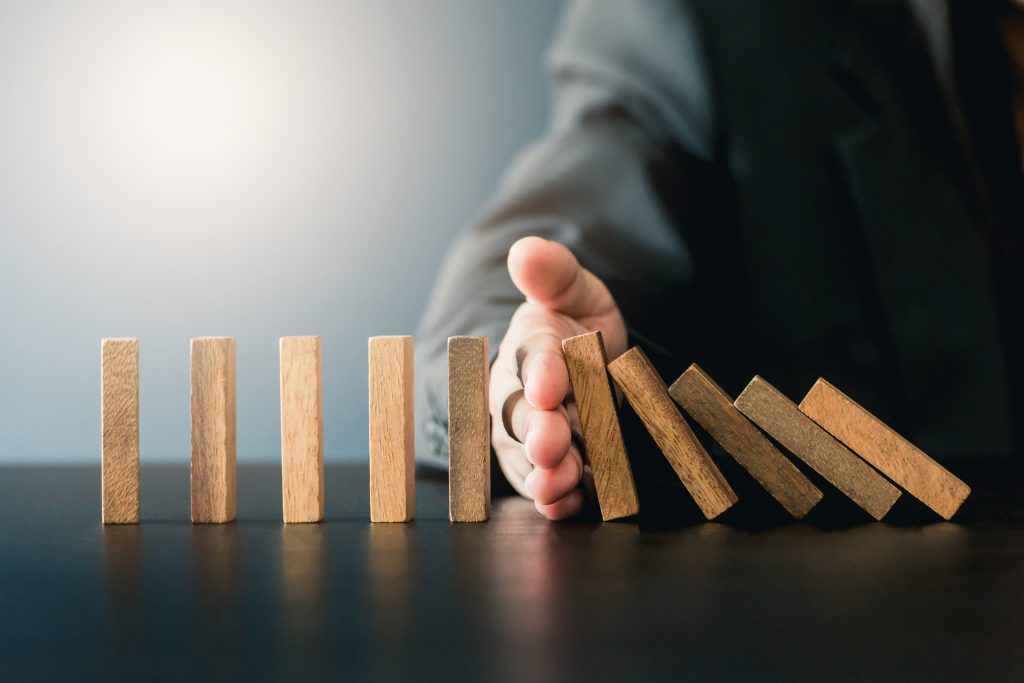 Close up of businessgirl hand Stopping Falling wooden Dominoes effect from continuous toppled or risk, strategy and successful intervention concept for business.